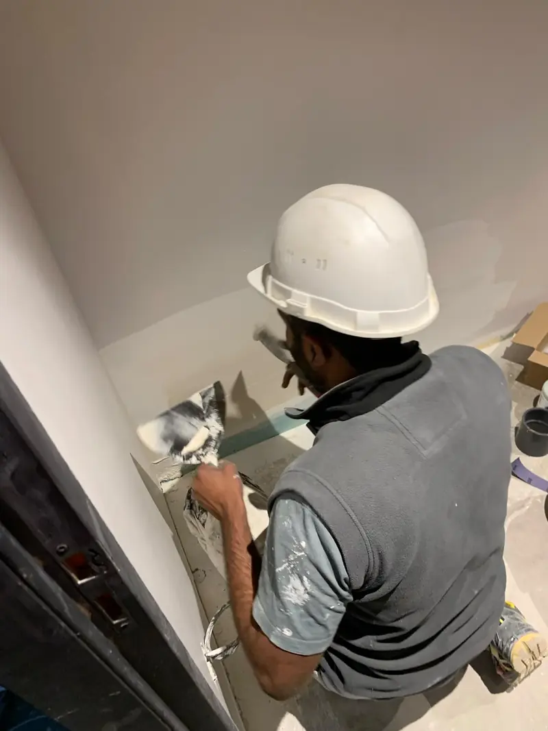 Ouvrier appliquant un enduit sur un mur, casque blanc